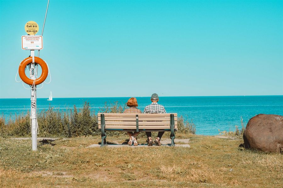 Senior couple on a bench overlooking blue water on a sunny day