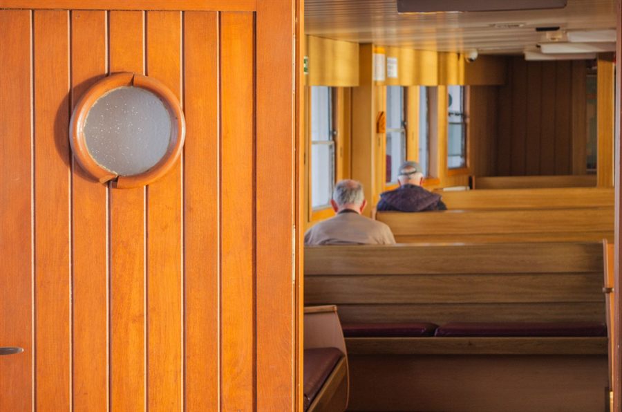 Older passengers seated in a warm wooden passenger saloon aboard a ship