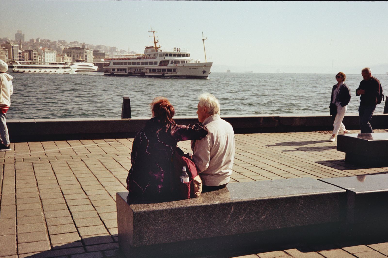 Senior couple sitting together on a waterfront bench watching passenger ships, dreaming of cruises for seniors