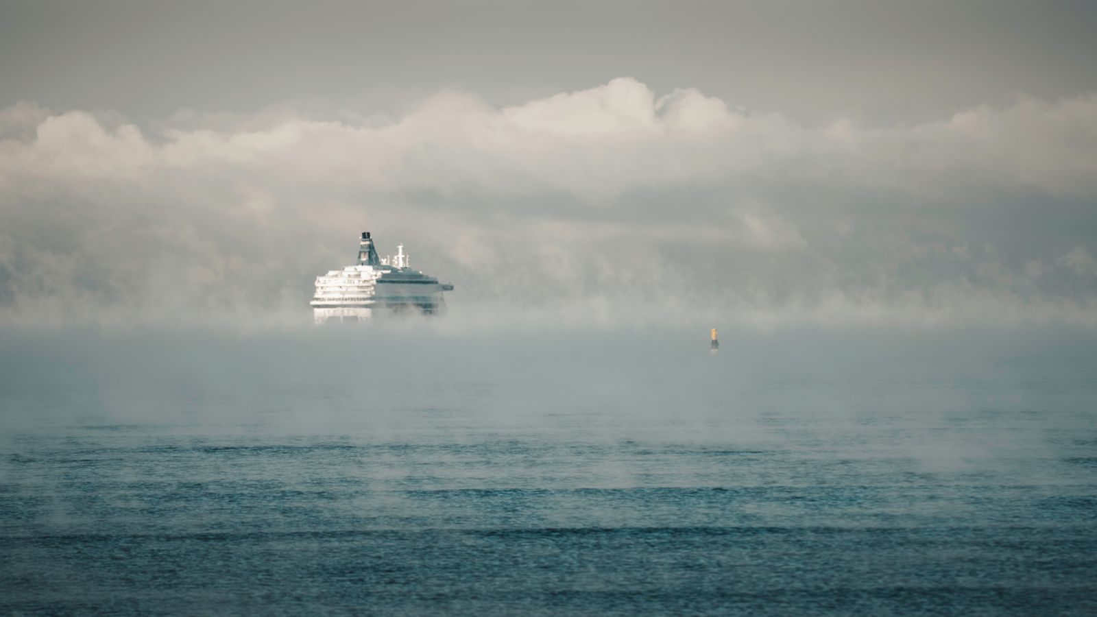 White cruise ship emerging from sea mist on a calm morning, recalling the golden cruise ship era
